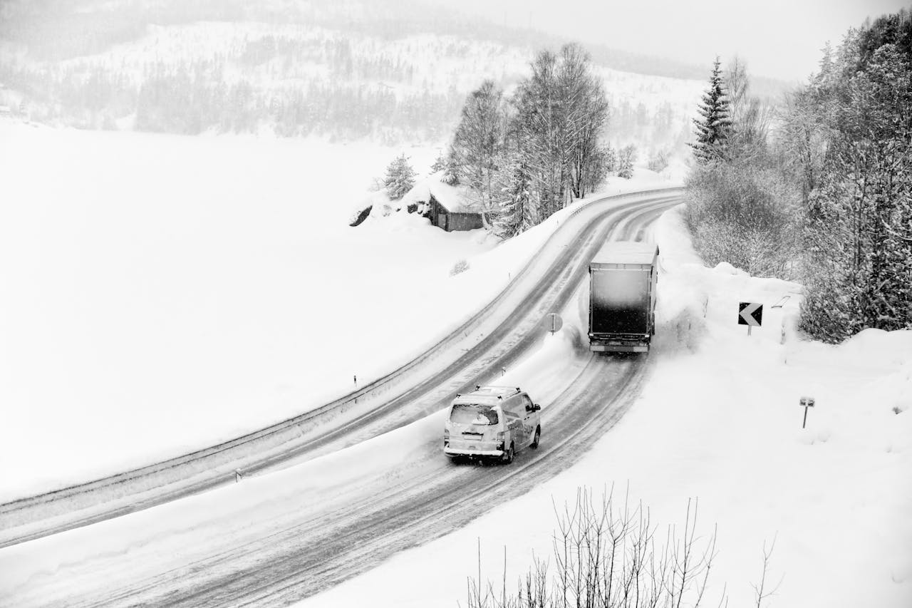 A black and white photo of a truck driving on a snowy road